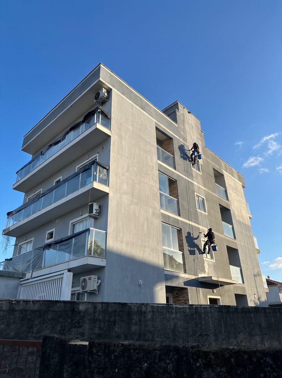 Dois pintores da Prime suspensos por corda pintando a fachada de um prédio de quatro andares