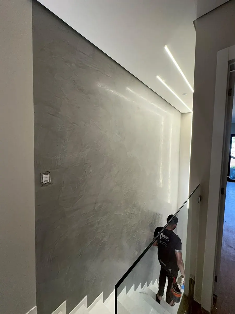 Aplicador da Prime finalizando parede de escada em cimento queimado cinza, com iluminação embutida