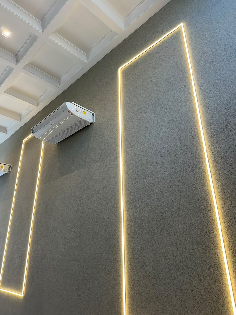 Parede revestida com pedras naturais em tom grafite, iluminada por fita de LED embutida