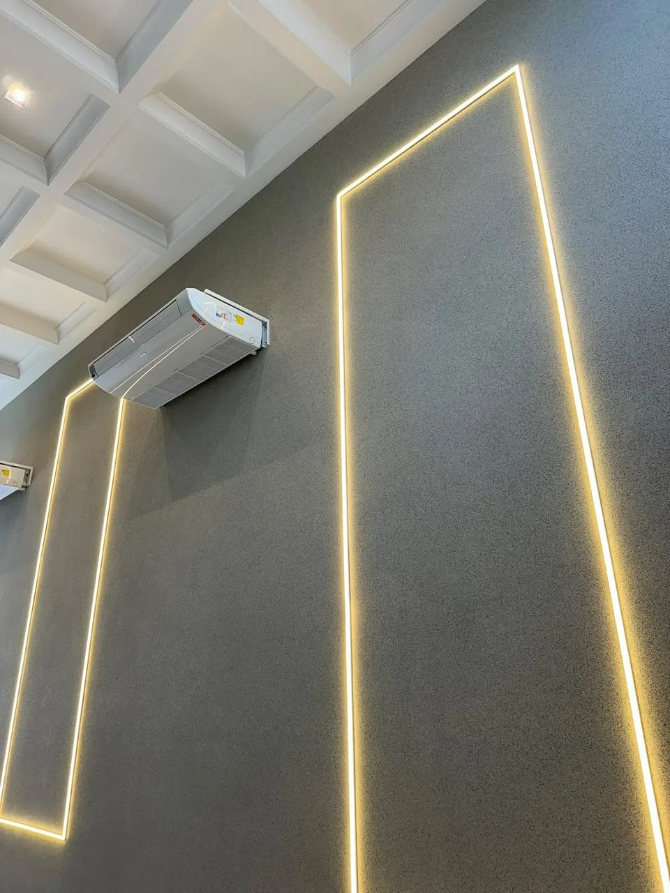 Parede revestida com pedras naturais em tom grafite, iluminada por fita de LED embutida