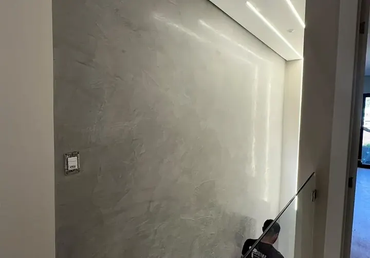 Parede de escada revestida em cimento queimado cinza, com aplicador da Prime finalizando o acabamento