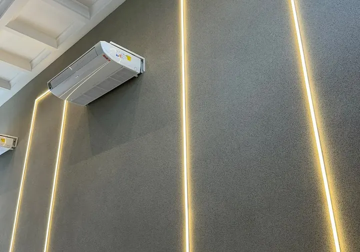 Parede revestida com pedras naturais em tom grafite, iluminada por fita de LED embutida